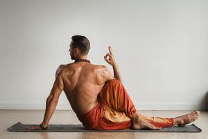 ein Mann mit ein nackt Torso tut Yoga drinnen. Fitness Trainer foto