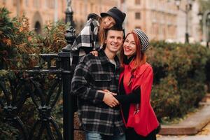 ein stilvoll Familie von drei Spaziergänge durch das Herbst Stadt posieren zum ein Fotograf . Papa, Mama und Tochter im das Herbst Stadt foto