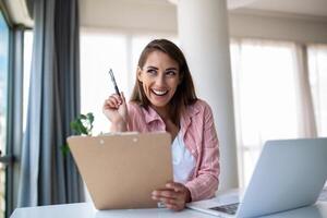 Remote-Job-, Technologie- und People-Konzept - glücklich lächelnde junge Geschäftsfrau mit Laptop-Computer und Papieren, die im Home Office arbeiten foto