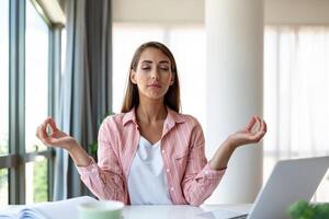 Ruhe Frau entspannend meditieren mit Laptop, Nein Stress kostenlos Linderung beim Arbeit Konzept, achtsam friedlich jung Geschäftsfrau oder Schüler üben Atmung Yoga Übungen beim Arbeitsplatz, Büro Meditation foto