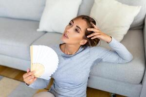 Frau setzt Kopf auf Sofa Kissen fühlt sich träge fällig unerträglich Hitze, Wellen Hand Ventilator cool Sie selber, heiß Sommer- eben ohne Klimaanlage Klima Steuerung System Konzept foto