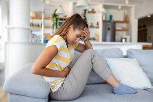 Frau, die auf dem Sofa liegt und im Wohnzimmer krank aussieht. schöne junge frau, die auf bett liegt und hände auf ihrem bauch hält. frau mit schmerzhaften bauchschmerzen im bett, menstruationsperiode foto