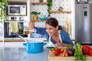 begeistert jung Dame Kochen und Probenahme Abendessen im ein Topf, positioniert im ein glatt Küche beim heim. Zuhause Exekutive vorbereiten gesund Küche mit ein Grinsen. Haushalt Verwaltung und Nährstoff Aufnahme. foto