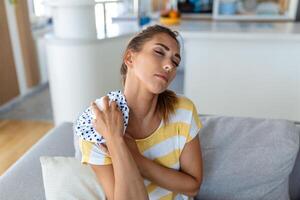 Schmerzen in der Schulter. oberarmschmerzen, menschen mit körpermuskelproblemen, gesundheits- und medizinkonzept. attraktive frau, die auf dem bett sitzt und mit einer anderen hand die schmerzhafte schulter hält. foto