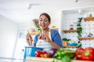 glücklich jung Frau Kochen Verkostung Abendessen im ein Topf Stehen im modern Küche beim heim. Hausfrau vorbereiten gesund Essen lächelnd . Haushalt und Ernährung. Diät Rezepte Konzept foto