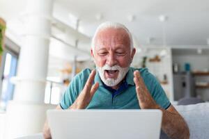 Alten Mann sitzend auf Couch suchen beim Laptop Bildschirm Schrei mit Freude fühlt sich aufgeregt glücklich feiern Lotterie Sieg, Glücklich Moment, habe online Gelegenheit, Der Umsatz und Rabatte E-Commerce Konzept foto