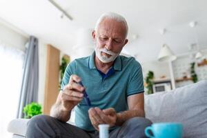 reifen Mann testen zum hoch Blut Zucker. Mann halten Gerät zum Messung Blut Zucker, tun Blut Zucker prüfen. Senior Mann Überprüfung Blut Zucker Niveau durch Glukometer und Prüfung Streifen beim Zuhause foto