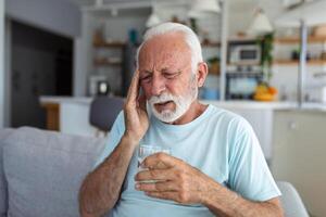 Senior Mann Leiden von ein Kopfschmerzen beim heim. besorgt Senior Mann Sitzung allein im seine heim. diese Kopfschmerzen Ja wirklich tut weh. meine Kopf ist Tötung mich foto