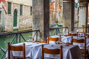 hölzern Tabellen auf eng Straße unter typisch bunt Häuser und klein Brücke im Venedig, Italien. foto