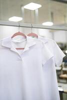 Neu Weiß T-Shirts hängen auf Kleiderbügel im ein Kleidungsstück Fabrik foto