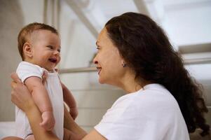 zärtlich jung Mama etabliert emotional Kontakt mit ihr Neugeborene Baby. lächelnd Mutter spielen mit ihr Kind foto