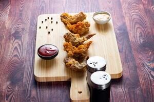 knusprig Hähnchen Flügel mit Tomate Soße und Mayo tauchen isoliert auf Schneiden Tafel Seite Aussicht von Fast Food foto