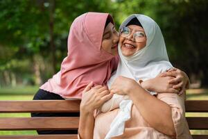 Muslim Vorsichtig Pflegekraft oder Krankenschwester nehmen Pflege von das geduldig im das Krankenhaus Park. glücklich Muslim Mutter im Hijab umarmen Tochter. Konzept von Ersparnisse und Senior Gesundheit Versicherung, ein glücklich Familie foto