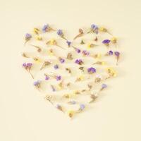 Herz gestalten gemacht von bunt trocken Blumen auf Pastell- Sahne Hintergrund. romantisch Blumen- Gruß Karte. minimal Liebe Konzept und Einfachheit. Natur dekorativ Design. eben legen. foto