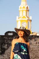 schön Frau tragen das traditionell kolumbianisch Hut namens Sombrero vueltiao beim das Uhr Turm auf das historisch Straßen von das Cartagena de Indien ummauert Stadt foto