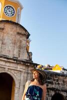 schön Frau tragen das traditionell kolumbianisch Hut namens Sombrero vueltiao beim das Uhr Turm auf das historisch Straßen von das Cartagena de Indien ummauert Stadt foto