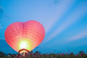 Herz geformt heiß Luft Ballon schwimmt Über Feld von Blumen im Abend, und Herz geformt Luftballons sind ebenfalls Symbol von Liebe und Freundschaft. mit Herz geformt Luftballons wie Symbol von Liebe und Freundschaft. foto