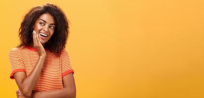 süß kreativ und feminin stilvoll afrikanisch amerikanisch jung weiblich im gestreift T-Shirt gelehnt Kopf auf Palme Blick links mit neugierig und bezaubernd Ausdruck entzückend Hören interessant Geschichte foto