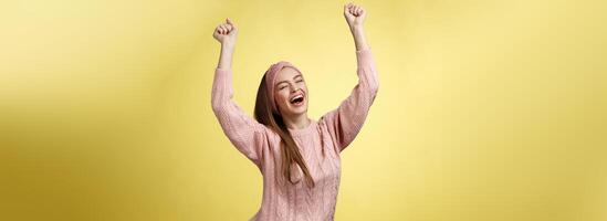 positiv feiern glücklich europäisch jung Frau tragen beiläufig Sweatshirt Geschrei glücklich schreien Ja, triumphierend Rennen Hände oben im Erfolg Springen begeistert Jubel fröhlich Über Erfolg foto