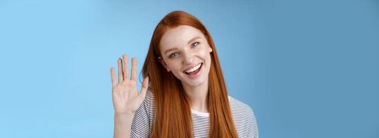 attraktiv zuversichtlich Rothaarige frech Mädchen rein sauber Haut Blau Augen kippen Kopf fröhlich winken Hand Hallo Hallo Geste Gruß Sie aussehen Kamera freundlich Begrüßung Freund, Stehen Studio Hintergrund foto