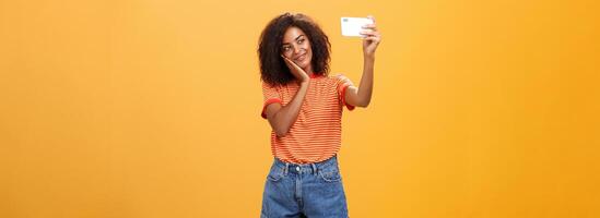 Frau gemacht bilden alle Tag zu Post Neu Foto online nehmen Selfie auf Marke Neu Smartphone Herstellung süß Gesicht gelehnt Kopf auf Palme lächelnd sanft beim Gerät Bildschirm posieren Über Orange Hintergrund