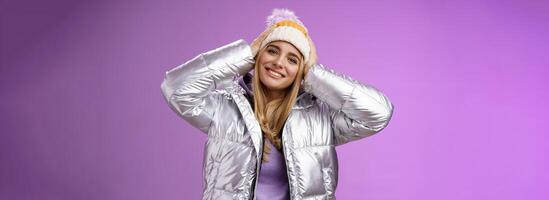 zärtlich romantisch attraktiv blond weiblich genießen Winter Ski Resort Ferien haben Spaß aussehen zufrieden lächelnd breit kippen Kopf berühren Hut tragen Silber stilvoll Jacke, lila Hintergrund foto