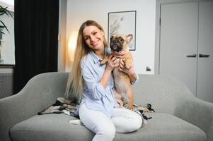 jung ziemlich Frau im beiläufig Kleider umarmen ihr Hund Sitzung auf das Sofa im das Leben Zimmer von ihr gemütlich Land Haus. Tier Kommunikation Konzept foto