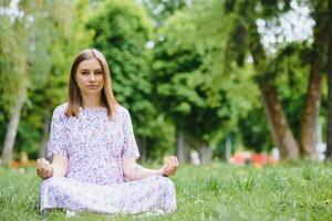 schwanger Frau tun Yoga im das Park. Sitzung auf das Gras. foto