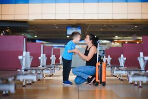 Familie beim Flughafen Vor Flug. Mutter und Sohn warten zu Tafel beim Abfahrt Tor von modern International Terminal. Reisen und fliegend mit Kinder. Mama mit Kind Einsteigen Flugzeug. Gelb Familie foto