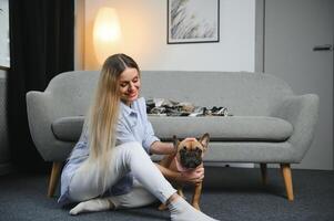 jung ziemlich Frau im beiläufig Kleider umarmen ihr Hund Sitzung auf das Sofa im das Leben Zimmer von ihr gemütlich Land Haus. Tier Kommunikation Konzept foto