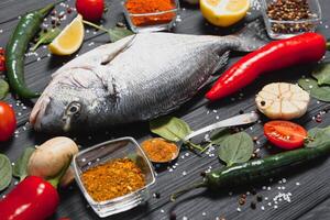 frisch roh Dorado Fisch auf Backen Papier mit Zitrone, Pfeffer, Tomaten und verschiedene Gewürze auf hölzern Hintergrund mit Kopieren Raum. foto