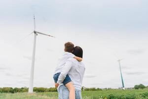 Mutter halten ihr Sohn im Natur. Wind Turbinen im das Hintergrund. foto