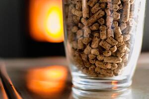 Pellet zum Herd oder Kessel im ein Glas, komprimiert Holz Pellet mit ein Herd im Hintergrund foto