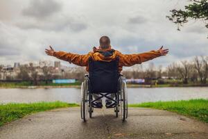 Rückseite Aussicht Bild von Paraplegiker behindert Mann im Rollstuhl durch das See. er ist genießen draussen. foto