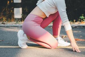 Fitness Konzept, ein Nahansicht Aussicht von ein Fitness Enthusiast im Rosa Gamaschen Dehnen ihr Beine auf ein Park Weg. foto