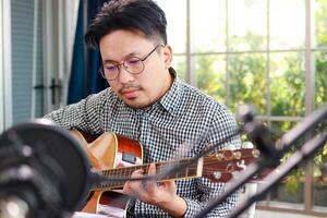 asiatisch Musiker Künstler sitzen und abspielen Gitarre im das Studio. Musik- Konzept. online Musik- Lektionen foto
