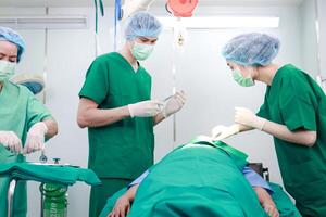 Fachmann Mannschaft von asiatisch Chirurgen ausführen Chirurgie auf ein geduldig Lügen auf ein Bett im ein Krankenhaus Betriebs Zimmer. medizinisch Konzepte. Notfall Chirurgie foto