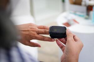 ein Alten Frau Maße Fingerspitze Sauerstoff durch Sie selber. Hilfe Monitor und Monitor Symptome von COVID-19. das Konzept von Patienten bleiben beim heim. foto