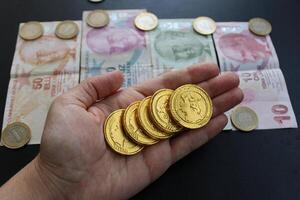 ein Hand hält ein Gold Münze mit das Wort Drachen auf Es. Türkisch Banknoten im das Hintergrund foto