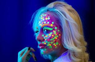 Porträt von ein Frau mit gemalt Gesicht, Frau mit uv bilden im Studio, Porträt von ein Frau im Karneval Maske, das Frau ist dekoriert im ein ultraviolett Pulver foto