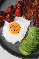 gesund Frühstück mit gebraten Ei, Speck, Avocado und Kirsche Tomaten foto