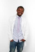 glücklich schwarz Arzt Mann mit klein Bart im Weiß Mantel, hell Shirt, Krawatte und Jeans, Weiß Hintergrund foto