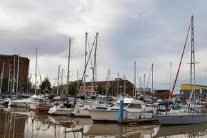 Segelboote festgemacht beim ein still Yachthafen mit Ruhe Wasser und wolkig Himmel, reflektieren Masten auf das Wasser Oberfläche. foto
