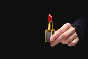 rot Lippenstift im ein Frau Hand auf ein dunkel Hintergrund. Mädchen halten ein Beliebt kosmetisch Produkt foto
