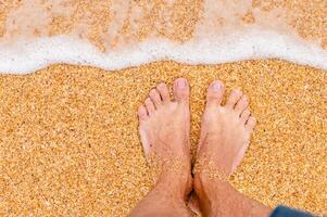 oben Aussicht von männlich Beine im Blau kurze Hose auf golden Sand im Sonnenlicht. suchen Nieder beim ein Mann im kurze Hose Stehen auf das Meer sandig Strand foto