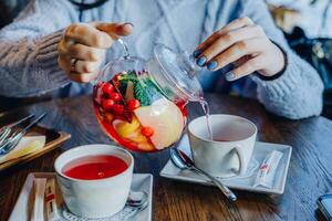 Frau Gießen Tee von ein Teekanne in ein Glas Tasse. foto