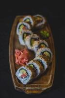 Sushi Rollen auf ein hölzern Teller auf ein schwarz Hintergrund. japanisch Essen foto