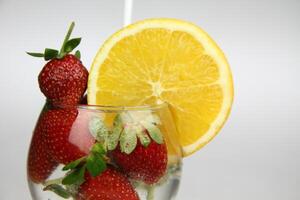 ein Glas von Wasser mit Erdbeeren und ein Orange Scheibe foto