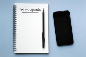 heute Agenda geschrieben auf Notizbuch mit Stift und Smartphone auf Blau Hintergrund. foto