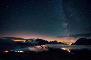 Fernlichter kommen auf der linken Seite. schöner raum voller sterne am himmel. die Berge sind von dichtem Nebel umgeben foto